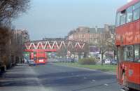 Seeing orange; a northbound train heads over Great Western Road and into Anniesland station while four buses head west. The noticeable dip under the bridge is due to the roadway having been lowered and the original bridge replaced to allow double deck trams to pass underneath. <br><br>[Ewan Crawford /02/1991]