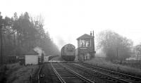 A misty morning on the Waverley route at Kershopefoot in the 1960s as an EE Type 4 accelerates through the station and over the level crossing with a northbound freight, just prior to crossing the Kershope Burn. In this case the photographer is standing in Scotland with the freight still in England. [See image 27856]<br><br>[K A Gray //]