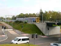 The 12.48 Edinburgh Waverley - Bathgate service pulls away from the westbound platform at Uphall on 13 October and is about to cross the recently opened replacement bridge over the widened B8046 road. An entrance has now been formed on the left into the area on the north side of the station where additional car parking will be provided.<br><br>[John Furnevel 13/10/2010]