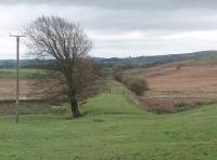 The old route from Low Gill to Clapham is visible for much of its length, despite being finally closed in 1966. Here though a section of trackbed near Clapham disappears briefly into the fields. Behind the camera an overbridge carrying the B6480 from Bentham has been removed and the cutting beyond is occupied by a small campsite. View southeast from point SD 721693 towards Clapham station and the surviving Settle Junction to Carnforth line. [See image 21813] <br><br>[Mark Bartlett 23/10/2010]