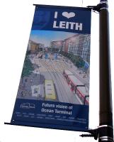 Attached to various lampposts along Leith Walk are banners depicting scenes or people connected with Leith. This one shows a future vision of Ocean Terminal, currently a busy bus terminus (among other things). The artist must have a vivid imagination, as it shows trams actually in operation. The trackwork has an M C Escher like quality, at one point rising up to become twin overhead wires (over a single track) without supporting poles. Too clever for me.<br><br>[David Panton 03/01/2011]