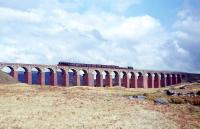 April 1965, just two months before closure of the 'Port Road' direct line from Dumfries to Stranraer. A Stranraer-bound mixed freight train headed by a Stanier 'Black 5' crosses the Big Water of Fleet viaduct westbound against a backdrop of bleak Galloway mountains and moorland. The viaduct still survives as a listed structure, but a 1990s' proposal by Dumfries & Galloway Regional Council for a new Trans European Network rail link to Stranraer, as an alternative to upgrading the A75 road, came to nothing.<br><br>[Frank Spaven Collection (Courtesy David Spaven) /04/1965]