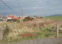 Looking east towards Campbeltown from Machrihanish station site along the old trackbed, which is still clearly visible behind the houses on the main road, almost eighty years after final closure. Further east, where the line crossed farmland, its course is much less well defined and large parts have disappeared altogether. [See image 33498] for a map of the station site and approaches in 1921. <br><br>[Mark Bartlett 26/03/2011]