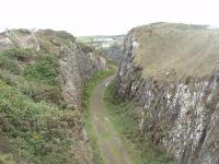 The Portpatrick branch rose steeply onto the headland from the terminus before looping round and continuing the climb over the moors to Stranraer Town. For anyone in Portpatrick with half an hour to spare the walk through the rocky cutting on the headland and then back along the cliff top path seen here is highly recommended. View towards Portpatrick at Map Ref NX 003535. [See image 33026] for an OS map of the branch prior to closure in 1950.<br><br>[Mark Bartlett 27/05/2011]