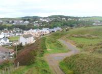 A view from Portpatrick headland along the old trackbed towards the terminus in May 2011. This is where the branch emerged from the clifftop cutting and curved round as it dropped towards the station at the head of the small valley. An underbridge was still in place by the large house when the 1999 OS map was printed but has since been removed for the access track seen here. The line closed completely in 1950. <br><br>[Mark Bartlett 27/05/2011]