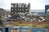 Site of the former Caledonian Leith East goods station seen looking north towards the docks in August 2011, with the vacant yard on the near side of the red brick wall [see image 35359]. Beyond the tenement on the other side of Salamander Street stood the NB South Leith goods station [image 30277], while the pile of scrap in the left background stands on the the original Edinburgh & Dalkeith route to South Leith passenger station [image 27583]. Rails can still be seen imbedded in the cobbles of Salamander Place on the left [image 3175].    <br>
<br><br>[Bill Roberton 23/08/2011]