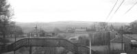 View north from the tall signal box at the south end of Reedsmouth station on 9 November 1963. The photograph was taken during a photostop on the RCTS/SLS <I>'Wansbeck Wanderer'</I> railtour. The Border Counties line to Riccarton Junction runs off to the left through rural Northumberland towards Bellingham. The line is seen passing the former locomotive shed, officially closed in 1952 when a sub to 52C Blaydon. On the right is the station approach road from the hamlet of Redesmouth on the River Rede (note the spelling). Off picture to the right is the Wansbeck Valley platform, at which Ivatt 2-6-0 no 43129 is standing with the special. For the view south from the signal box at this time [see image 23266] <br><br>[K A Gray 09/11/1963]