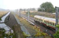 View east at Forrestfield on a wet and overcast 20 September as the 11.27 Milngavie - Edinburgh Waverley runs through the site of the former station. What at first glance might look like a new stretch of canal on the left (until you notice the digger in the distance) is the rain soaked cycle path/walkway built to replace that which the railway has recently taken back. [See image 26557]<br><br>[John Furnevel 20/09/2011]