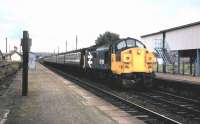 37035 with a southbound train at Muir of Ord in 1985. The now demolished station building stands in the left background, with part of the former grain transhipment facilities on the right [see image 16157].<br><br>[Colin Miller //1985]