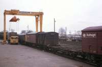 A typical scene at Elgin freight depot in the late 1970s - a BR lorry waits to offload a container of whisky casks for Central Scotland while a Class 24 draws a rake of conventional and container wagons into place under the depot's gantry crane.<br><br>[Frank Spaven Collection (Courtesy David Spaven) //]