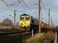 Freightliner 66557 stands on the up fast just south of Farington Junction on 27 November 2011 with switch and crossing carriers, some in the 'transit' position and some at the rear which are still horizontal awaiting the Kirow cranes to come and collect the panels. The activity was associated with the relaying of Farington Junction. To the left of the railway is the Lancashire Enterprises Business Park, part of which was engulfed in flames on 21 December 2011,  resulting in closure of the WCML.<br>
<br><br>[John McIntyre 27/11/2011]