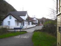 Looking west along the trackbed towards Morfa Mawddach in December 2011 from alongside the former Penmaenpool Station signalbox [see image 13937]. The surviving signal post and arms still stand alongside the old station master's house, ticket office and waiting room building, complete with hanging 'Platform 1' sign. The road ahead, once a level crossing, runs onto a toll bridge off to the right, linking with the north side of the Mawddach Estuary. <br><br>[David Pesterfield 07/12/2011]