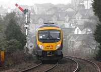 A murky morning at Grange-over-Sands as 185144 leaves for Barrow-in-Furness on a working from Manchester Airport. The image was taken from the park footpath that borders the line just west of the station. The <I>Whistle</I> board by the semaphore is for the boarded foot crossing that affords access to the promenade. [See image 31260].<br><br>[Mark Bartlett 12/02/2012]