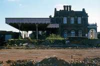 Unseen since the 1970s has been this Witham-facing elevation of Maldon East station. At the time of this photo in 1977, foundations were being laid (visible in the foreground) for a large timber storage shed which soon blocked the view. Part of the platform had also been cut away to make room. By the 21st century, the attractive station building, though still extant, had become hidden away within a cluster of industrial units. [See image 41272]<br><br>[Mark Dufton 13/11/1977]