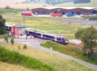 An Edinburgh - Inverness train runs east over Blackford level crossing, Perthshire, in July 2006. The 'Highland Spring' water bottling plant stands in the background.<br><br>[John Furnevel 07/07/2006]