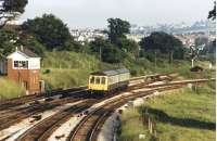 A summer evening in 1985, prior to the removal of Aller Junction, sees a DMU leave the Paignton branch and cross over the line to Totnes and Plymouth to run into Newton Abbott. With the junction removed there is no connection now and the lines run in parralel up to Newton Abbott station whilst colour lights have replaced the semaphore signals.<br><br>[Mark Bartlett /07/1985]