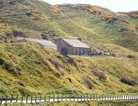 More than 60 years after closure, the old Macduff locomotive shed still stands on the hillside to the west of the former station [see image 39268], where it is now used for storage. The stone built 2-road straight shed, latterly a sub to 61A Kittybrewster, serviced locomotives between 1872 and 1951. Photographed in May 2012 looking south from the A98.<br><br>[John Furnevel 23/05/2012]