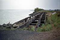 One of the last remaining structures on the Wivenhoe-Brightlingsea branch was this waterside trestle bridge on the approach to the terminus. It can be easily appreciated how the line became so severely damaged in the 1953 floods, taking months to repair. The view is towards Wivenhoe in August 1976.<br><br>[Mark Dufton 30/08/1976]