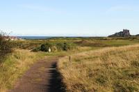 The trackbed of Brand's railway, Bamburgh, in September 2012. The 3 ft gauge railway ran from Kittling Hill whinstone quarry to Budle Pier. View south east with the track bed curling around to Kittling Hill. The fairway for the par 5 third hole is 10m to the right. Club house in the left distance with Bamburgh Castle seated on the massive whinstone outcrop on the right. The railway, which utilised steam locomotive haulage, closed during WW1. <br><br>[Brian Taylor 22/09/2012]