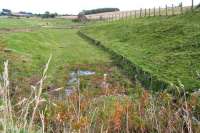 The trackbed of the Berwickshire Railway heading east from Greenlaw towards Duns on 6 October 2012. Note the remains of the wooden supports forming a low retaining wall along the north side of the cutting at this point. View from the realigned A6105 road [see image 40779].<br><br>[John Furnevel 06/10/2012]