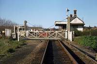 Looking north east over the level crossing towards Felixstowe Beach station in April 1977, around a decade after the passenger service (latterly summer season only) had ended. The wooden station building was eventually demolished on Easter Sunday 2004 despite attempts being made to list it for its architectural and historical merit. The line is still very busy with container traffic to the port.<br><br>[Mark Dufton 09/04/1977]