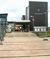 The south passenger entrance to Edinburgh Park station on 12 May 2013, with two sets of tram rails now crossing the pedestrian pathway between the road and the station. (The tram stop is just off picture to the right [see image 43099].) Standing at the eastbound platform is the 0755 Helensburgh Central - Edinburgh Waverley.<br><br>[John Furnevel 12/05/2013]