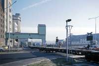 A rake of container flats hauled by 08661 holds up road traffic as it emerges from Ipswich Lower Yard and heads off through the docks complex to collect a load from Cliff Quay. It is a very cold morning in December 1985. Despite an upgrading of the dock line and lower yard facilities in the early 1980s to better handle container traffic, Felixstowe stubbornly held on to its virtual monopoly of this business. The lower yard and docks line finally succumbed to permanent <I>Network Change</I> (a euphemism similar to <I>reshaping</I>) in 2009 after a long period of inactivity.<br><br>[Mark Dufton /12/1985]