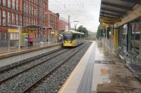 The tram stop at Shaw and Crompton has been constructed on the Oldham side of the level crossing next to Briar Mill. On 31 July 2013 a Manchester bound tram waits to depart. <br><br>[John McIntyre 31/07/2013]