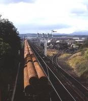 A trainload of pipes bound for the cement-coating plant near Invergordon heads north from Inverness in 1978 - the harbour branch and coal yard are to the right, with Ben Wyvis in the far distance.<br><br>[David Spaven //1978]