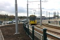 Curving away from the original railway alignment onto the new Oldham town centre street running section a Manchester bound service approaches the new Mumps interchange. The short lived and now redundant level crossing, closed in January 2014, can be seen beyond the new landscaping. [See image 44114] showing construction works at the same location in 2013.<br><br>[Mark Bartlett 13/02/2014]