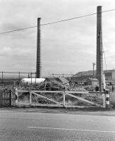 Looking north over the former level crossing that once took the NCB line to Woolmet Colliery (closed in 1966) over the A6095, photographed in the early 1980s [see image 46571].  The chimneys of Niddrie Brickworks dominate the scene. The whole area is now a shopping mall.<br><br>[Bill Roberton //]