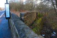 Looking east along the B981 Main Street, Lumphinnans, on 10 March. The moss covered stone wall and brickwork above it mark the railway boundary where the Cowdenbeath Old line burrowed beneath the road to reach Lumphinnans Central Junction.  The tunnel portal was at a lower level and is now buried.<br><br>[Bill Roberton 10/03/2014]