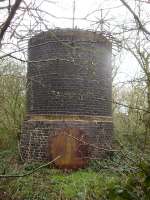 What is now believed to be the number 6 air shaft, located over the upside bore of Woolley Tunnel, is located just off Bramley Lane close to the top of the embankment alongside the M1 entry slip road from Woolley Edge southbound services. Of note is the bolt-on access panel and the fair degree of  distortion in the brickwork around the base section. A stone built air shaft, believed to be number 5 over the downside bore [See image 55837]  is sited at a lower level on the opposite side of Bramley Lane alongside the exit from the lorry parking area for the southbound services. A further stone built air shaft, believed to be number 2, again for the upside bore, sits alongside the M1 entry slip road from the northbound services, whilst a further two brick air shafts, numbers 7 & 8, have been located further south close to a pathway through the woodland running from this shaft, but I only noted number 8 when returning up some steps as it was well concealed by the extensive growth. Number 7 is also visible from the adjacent farmers field.    <br><br>[David Pesterfield 31/03/2014]