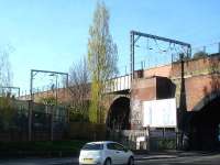 A section of 99 Arches Viaduct alongside Denby Dale Road, to the south of Wakefield Westgate in April 2014. The projecting structure behind the hoarding once housed the signal box controlling the junction with the branch to Wakefield Kirkgate. The signal with feather for the branch can be seen through the gantry to the left, with the junction itself located near the right hand gantry. <br><br>[David Pesterfield 18/04/2014]