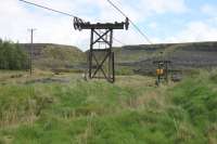 Inside the boundary of the clay pit at Claughton Moor the aerial ropeway runs at a much lower level. One of the shorter pylons can be seen here with a single wheel on the side carrying empty buckets and a double on the loaded side. View over the site fencing towards the loading area.  <br><br>[Mark Bartlett 09/05/2014]