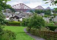 Looking south towards the Forth Bridge in June 2014. The North Queensferry (Old) branch emerged from a tunnel at the left and bisected the clump of trees in the background.  The houses to the left of the path are built on the in-filled cutting.  Exploration of the shrubbery to look for traces of the tunnel mouth will have to wait for the nettles to subside!<br><br>[Bill Roberton 10/06/2014]