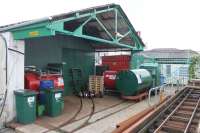 Hythe Pier tramway depot, as seen from the station platform. The 3rd rail of the <I>main line</I> track can be seen but the depot sidings are not electrified. Also in the picture is the spare loco and a railed diesel tank, used to supply fuel to the two Hythe ferry boats.. <br><br>[Mark Bartlett 25/05/2014]