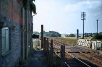 Bradfield station closed in 1956, but the building survived into the 1980s. This westward photo towards Mistley was taken from the short length of remaining platform on 15th August 1976, a day when eggs could be fried on car roofs. The crossing keeper has stripped to the waist to suit the conditions. Such was the low usage of the crossing (which was normally kept closed against the road), few were around to object to his attire. [Ref query 10473]<br><br>[Mark Dufton 15/08/1976]