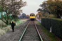 Scene at Clay Hills level crossing, Knodishall, on the Saxmundham-Aldeburgh branch on 1st November 1980. The RCTS railtour is returning from a visit to Leiston, and one of the crew is approaching to operate the gates. The train will soon reach the junction with the main line. Following closure to passengers in 1966, the line was retained to just beyond Leiston for Sizewell nuclear flask traffic. [Ref query 9825]<br><br>[Mark Dufton 01/11/1980]