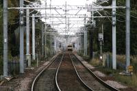 EMU 318266 on driver training at Baillieston, seen from the platform at Mount Vernon through the OHLE on 2 October. The railings on the upper left guard the abutments of the redundant overbridge which was removed to enable electrification. [See image 45923] for pre-electrification view.<br><br>[Colin McDonald 02/10/2014]