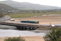 The welcome sight of a train running again from Pwllheli to Birmingham International. A class 158 DMU crosses the new concrete Pont Briwet on 17th October 2014, while in the foreground the old wooden trestle bridge standeth still. Difficulties in rerouting water pipes and BT cables have delayed demolition of this listed structure.<br><br>[Colin McDonald 17/10/2014]