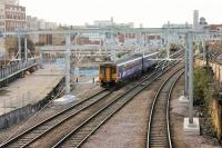 Wires getting nearer to Manchester Victoria in December 2014 as 156491 departs west past the site of Manchester Exchange, closed in 1969 and now being redeveloped. On the left is a small remaining section of Platform 3, which linked Victoria and Exchange from 1924 until closure. At 2194' in length it was Britain's longest platform. [See image 31084] taken from Platform 3 inside Exchange station in 1969. Postscript: Once the electrification was completed the parapets on the footbridge were raised and another handy railway vantage point was effectively removed.        <br><br>[Mark Bartlett 02/12/2014]