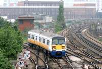 Good places not to have a derailment No.47 - Factory Junction. A Victoria - London Bridge via Peckham shuttle service passes on a murky July morning in 2005. Stewarts Lane shed is on the lower level beyond the trees on the left.  <br><br>[John Furnevel 21/07/2005]