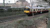 318250 passes the former Bridgeton Central Junction as it climbs east out of the cutting at High Street in February 2015. The trackbed of the old line to Bridgeton Central has seen some vegetation clearance recently, but much of the former route is still covered with the trees and shrubs which grew unchecked after the line was lifted in 1987. [See image 7978]<br><br>[Colin McDonald 03/02/2015]