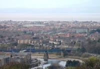 Crossing the River Lune in Lancaster is a DRS Class 66 heading a Daventry to Coatbridge container train. In this view of Carlisle Bridge from Williamson Park Morecambe Bay is clearly visible, as are the Furness hills beyond.<br><br>[Mark Bartlett 15/04/2015]