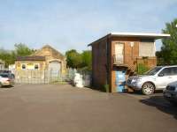 Looking east along the car park at Crewkerne Station on 11 May with the boarded up flat roof signal box seen at the end of the London bound platform, and the former goods shed further along to its left.<br><br>[David Pesterfield 11/05/2015]