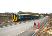 Construction workers make their way past the site of the former Cooke's Explosives factory to the Pont Briwet road bridge construction site on 13 April 2014 as the 1410 departure from Penrhyndeudraeth overtakes on its way to Birmingham International. The rail bridge was opened on 1st September 2014 and the new road bridge is finally set to open on Monday 13th July after various delays beset the project.  <br><br>[Colin McDonald 13/04/2015]