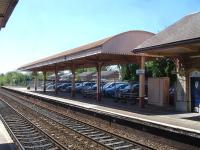 A long barrel roofed full width canopy stands to the south of the main upside building at Yatton station, as seen in this view from the opposite platform on 9 May. It previously also served the in-filled south facing Clevedon Branch bay, where cars can now be seen parked, upto closure of the branch to passengers on 3 October 1966.<br><br>[David Pesterfield 09/05/2015]