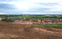 View south over the construction site on 12th July 2015. The OHLE, track work and ballast have been removed and work is proceeding to construct the bridge abutments on the north side of the line. In the foreground, work has started to realign Bredisholm Road with a new accommodation bridge over the A8 and M8.<br><br>[Colin McDonald 12/07/2015]