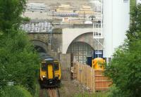 The shape of things to come at the south end of the Farnworth tunnels on 17 July 2015. A Preston to Hazel Grove service slowly exits the down tunnel which is currently be used in both directions, with the up tunnel sealed for filling with foam concrete. The shape of the new tunnel that will be bored can be seen disappearing behind the silo on the right.<br><br>[John McIntyre 17/07/2015]